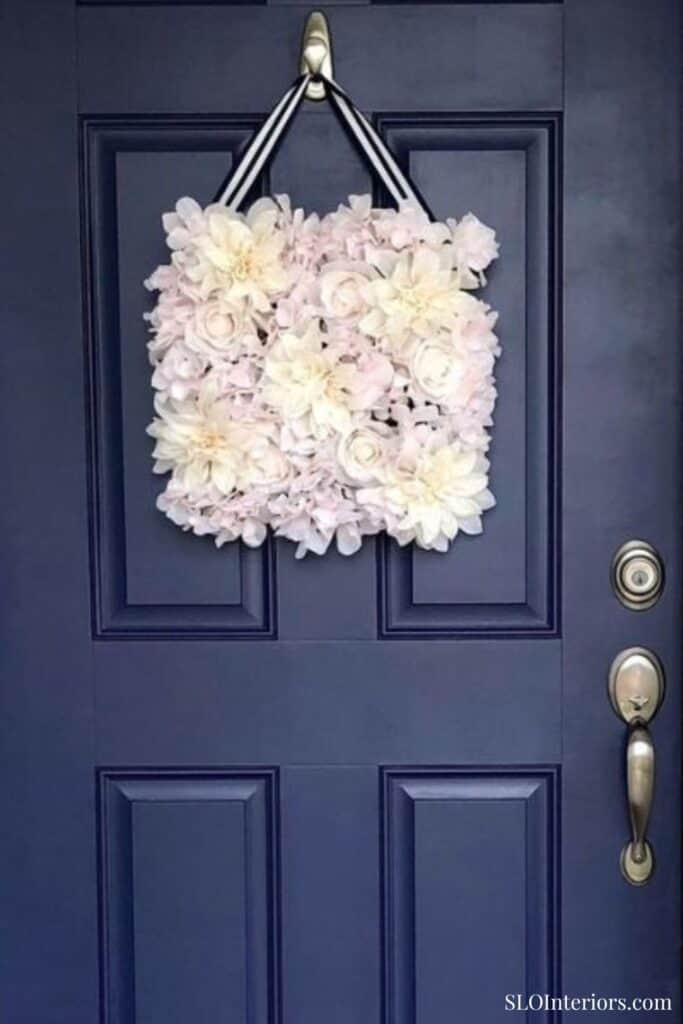 Beautiful floral wreath hanging on a navy blue door, decorative home interior accessory.