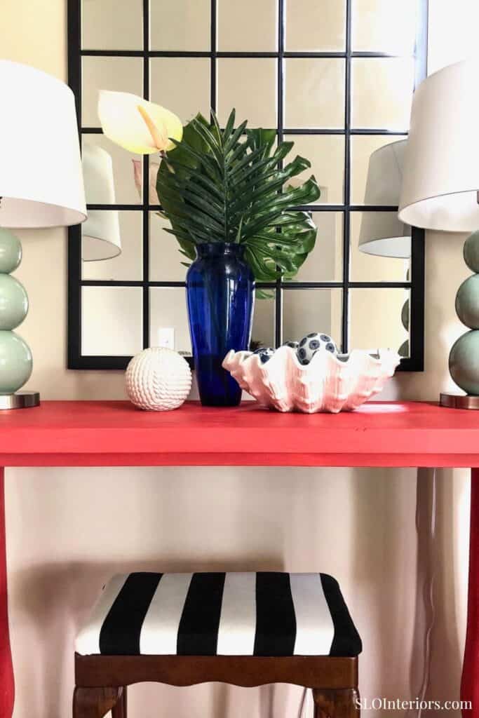 Elegant home decor with blue vase, tropical leaf, and shell centerpiece on red table.