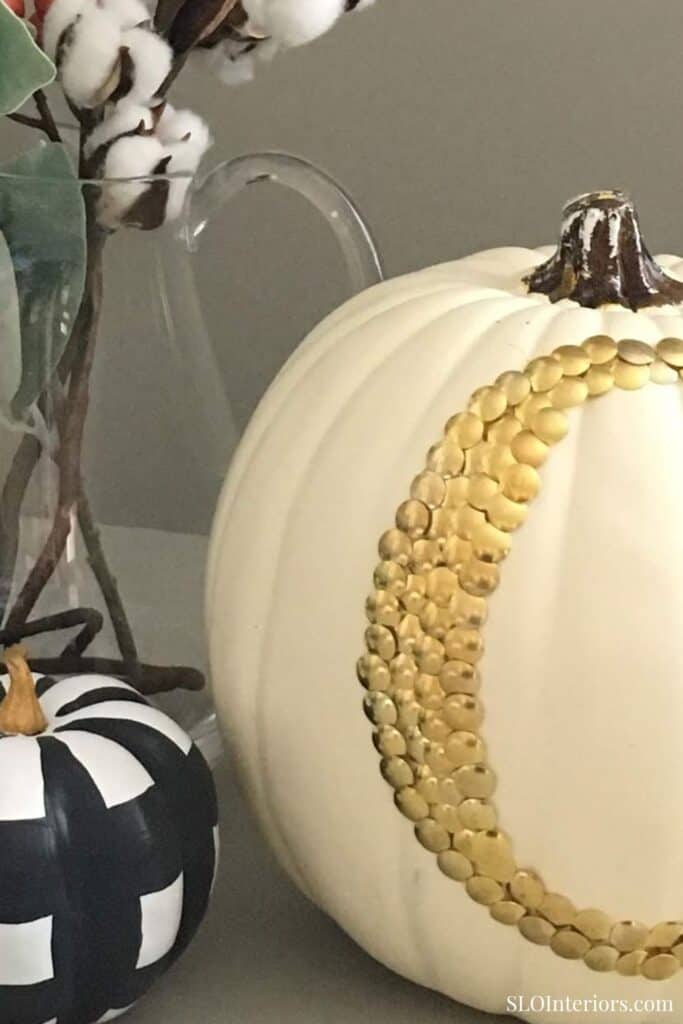 A pumpkin decorated with gold beads and a black and white checkered pumpkin, suitable for fall decor.