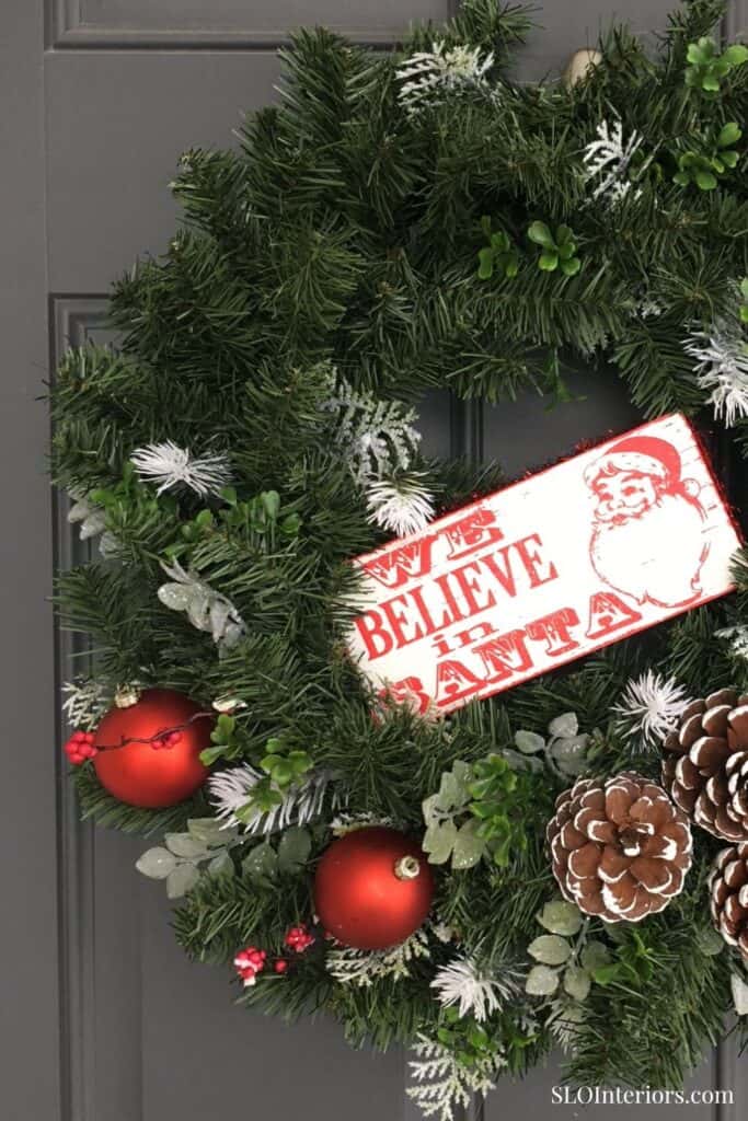 Festive Christmas wreath with pinecones, ornaments, and holiday decorations on door.