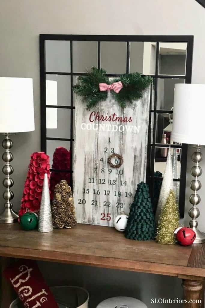 Festive Christmas decor with ornaments, greenery, and countdown calendar on wooden table.