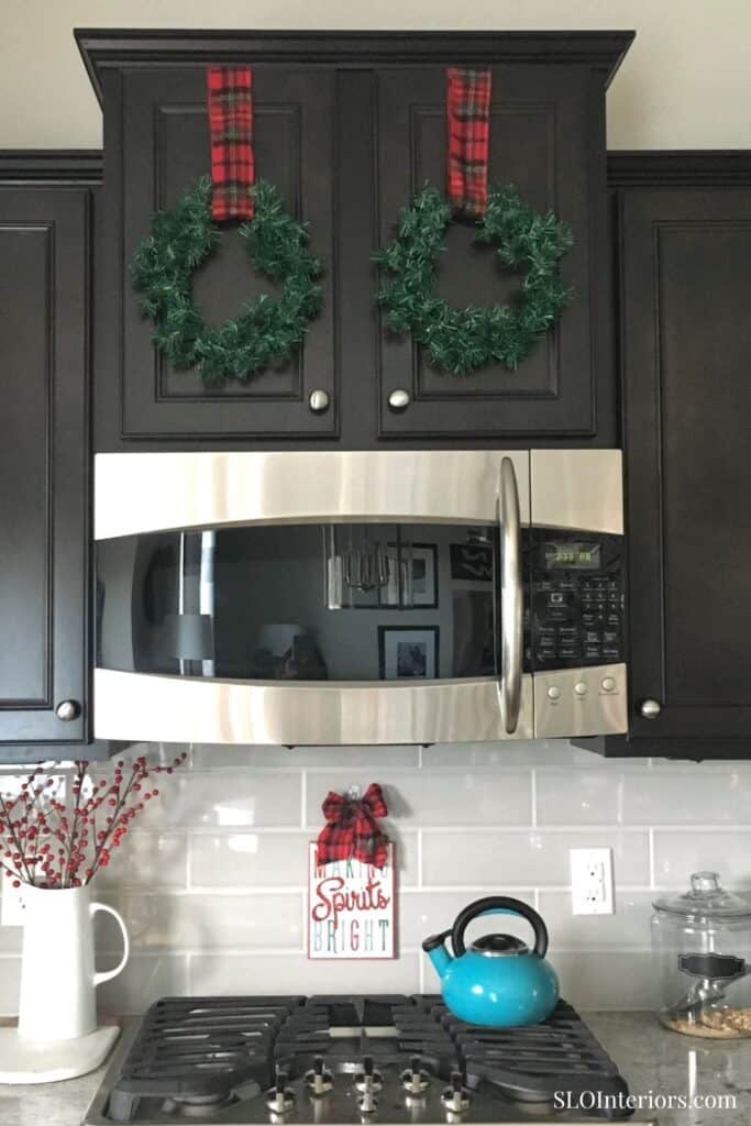 Festive kitchen with holiday wreaths, red ribbons, and a bright blue kettle.