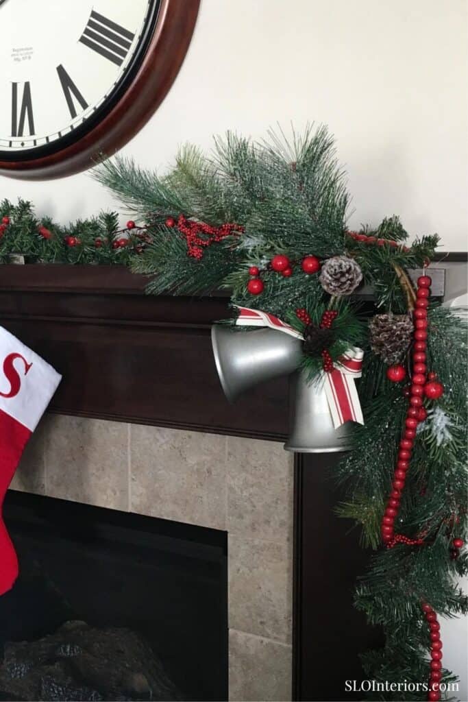 Festive Christmas garland with pine branches, red berries, and ornaments on fireplace mantel.