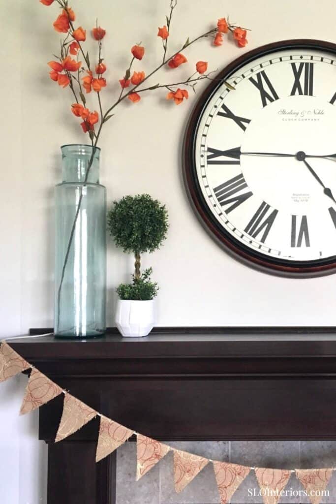 A lush green potted plant and orange flower branch decor with a large wall clock in a stylish interi.