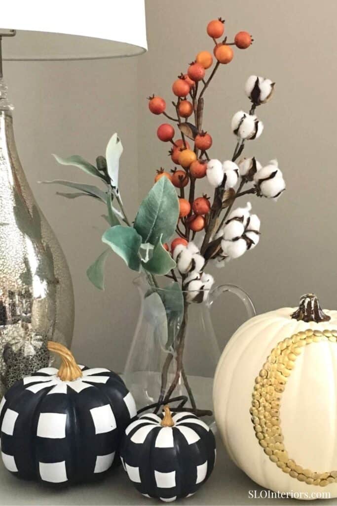 Decorative autumnal floral arrangement with pumpkins and cotton stems in a glass vase.