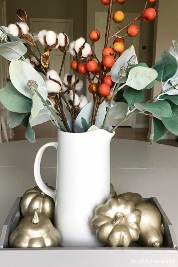 A lush autumnal floral arrangement with cotton, berries, and eucalyptus in a white pitcher.