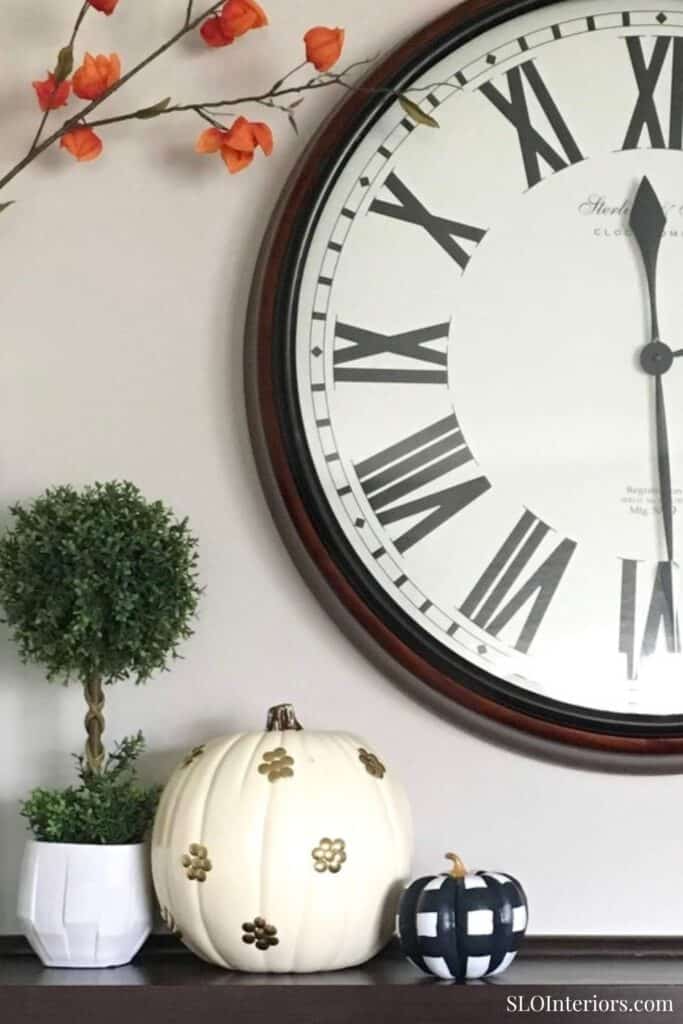 Elegant wall clock with floral decor and pumpkins for home interior design.