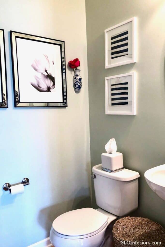 A modern bathroom with framed artwork, decorative wall accents, and a cozy rug.