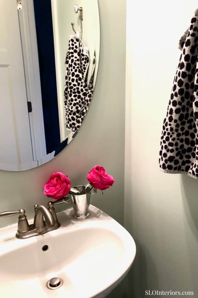 A stylish bathroom sink area with a mirror, polka dot towel, and pink roses in a silver vase.