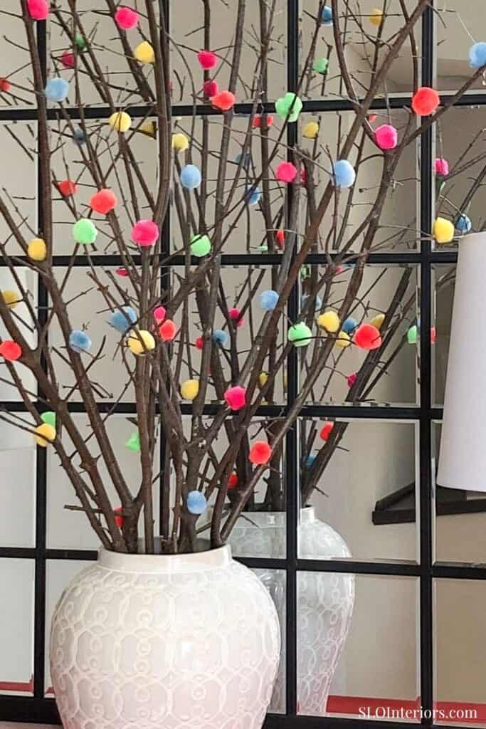 close-up of white urn with sticks and color pom poms centerpiece