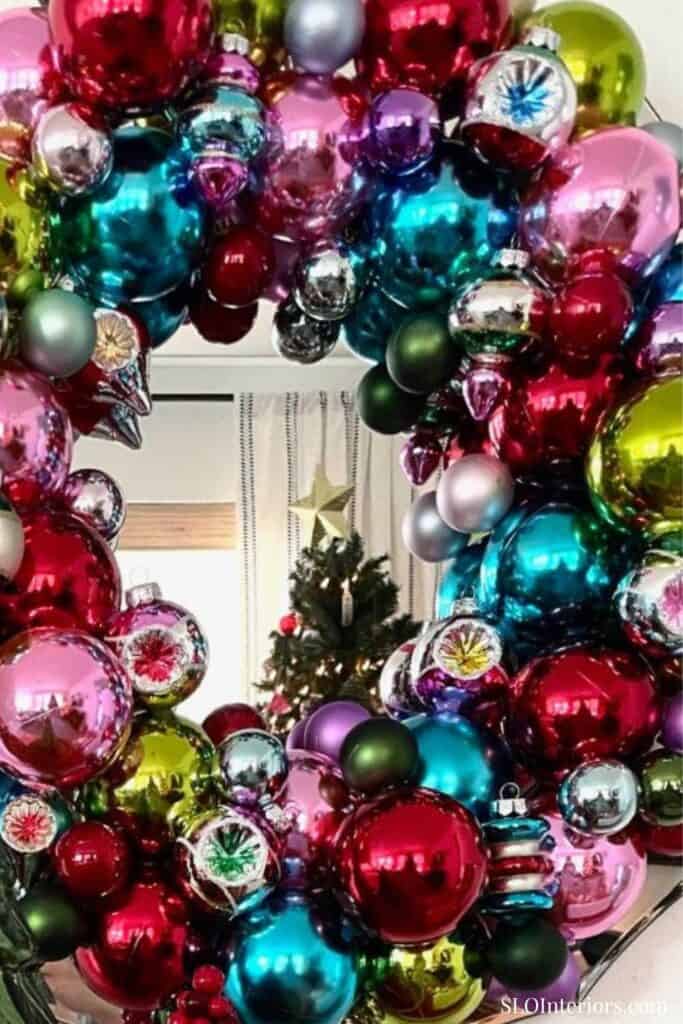 Festive Christmas wreath decorated with colorful ornaments and a Christmas tree in the background.