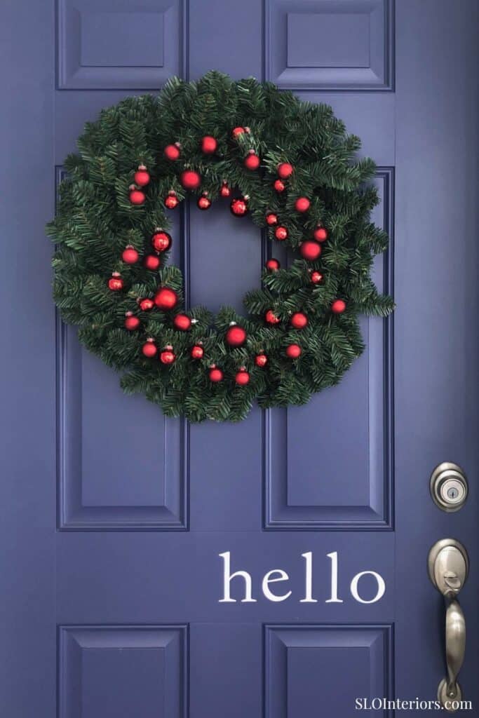 Festive holiday wreath with red ornaments on a blue door, welcoming greeting.