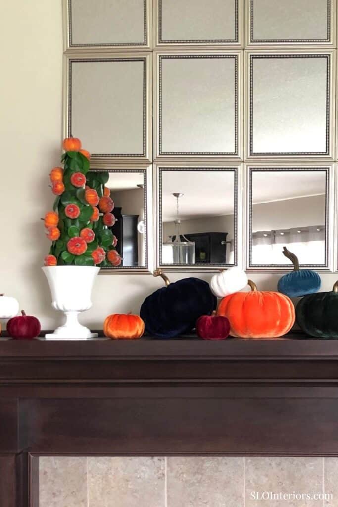 Elegant fall decor with pumpkins and flowers on dark wooden mantel in living room.