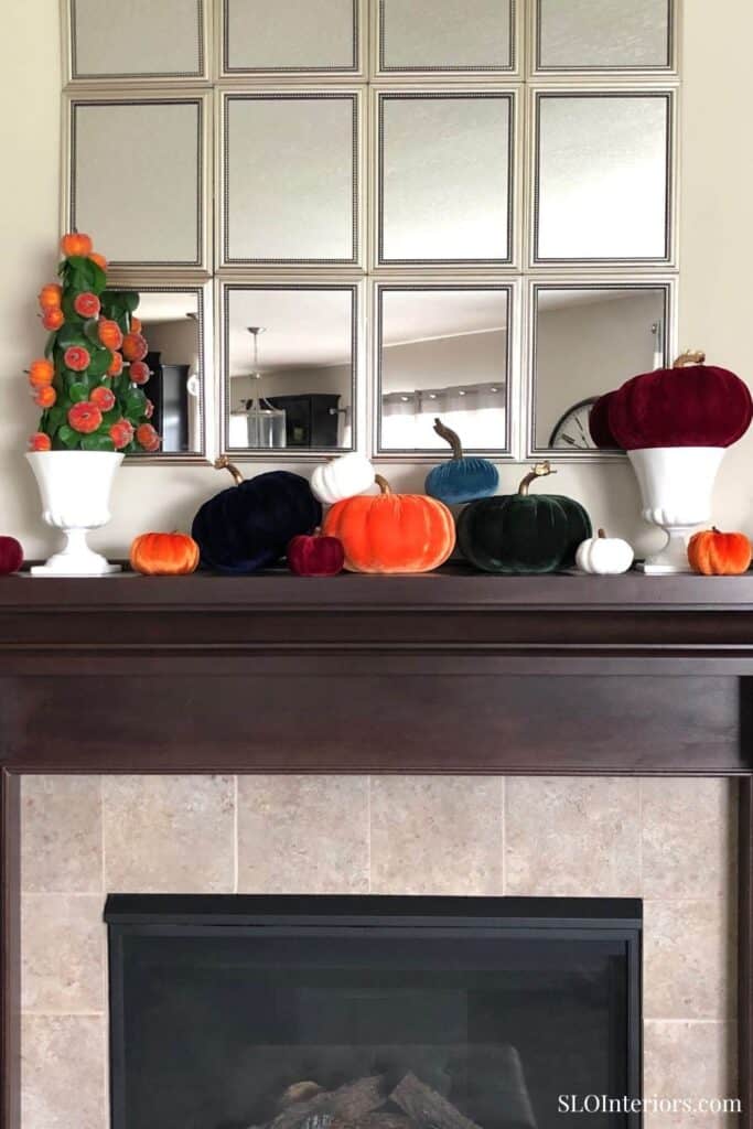 A colorful autumn-themed display with pumpkins and gourds on a fireplace mantel.