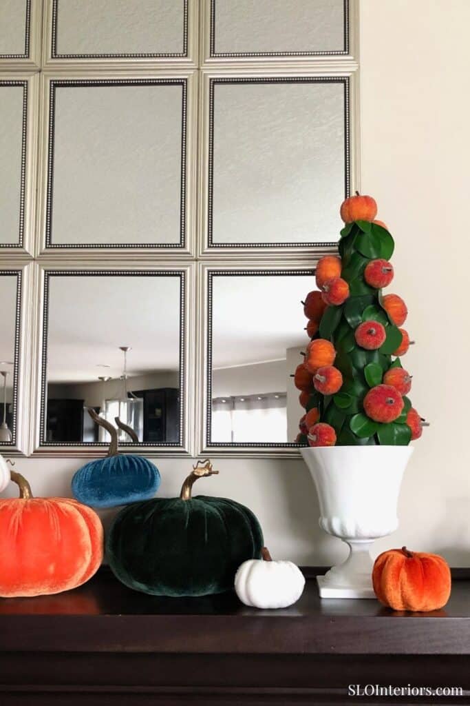 A colorful autumn-themed floral arrangement with pumpkins and gourds in a white vase.