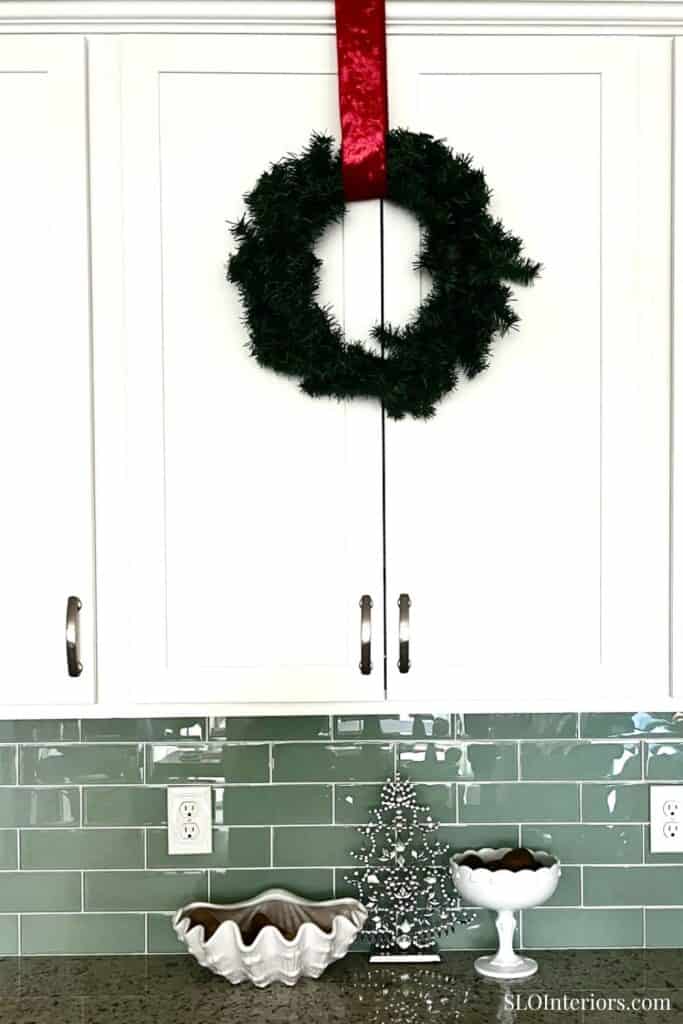 A festive green wreath with red ribbon hanging on white kitchen cabinets, holiday decor.