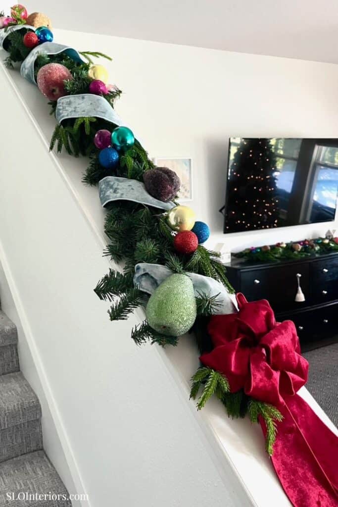 Festive Christmas garland with ornaments and red bow on staircase railing.