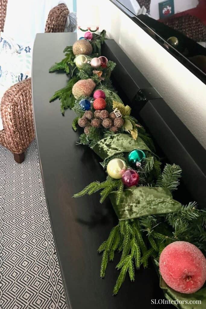Festive holiday garland with ornaments and greenery on black console table.
