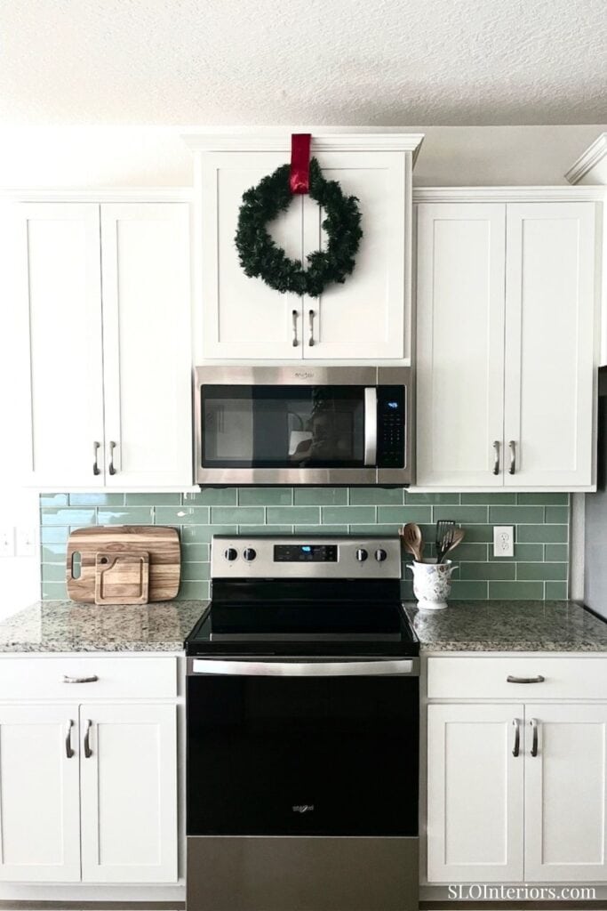 A cozy kitchen with white cabinets, green tile backsplash, and holiday decor.