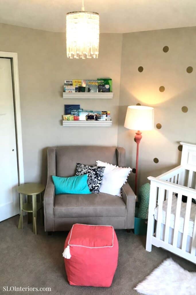 Modern nursery with gray sofa, white crib, colorful pillows, and wall decor.