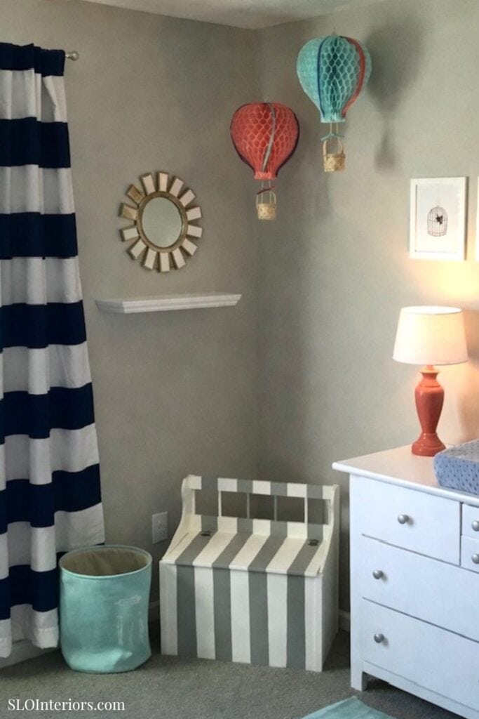 Cute nursery room with striped curtains, hot air balloon decor, and white furniture.