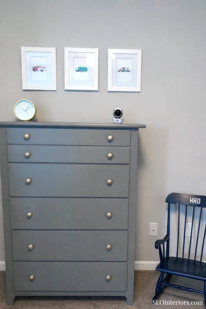 A modern gray dresser with framed artwork and a black chair in a stylish interior setting.