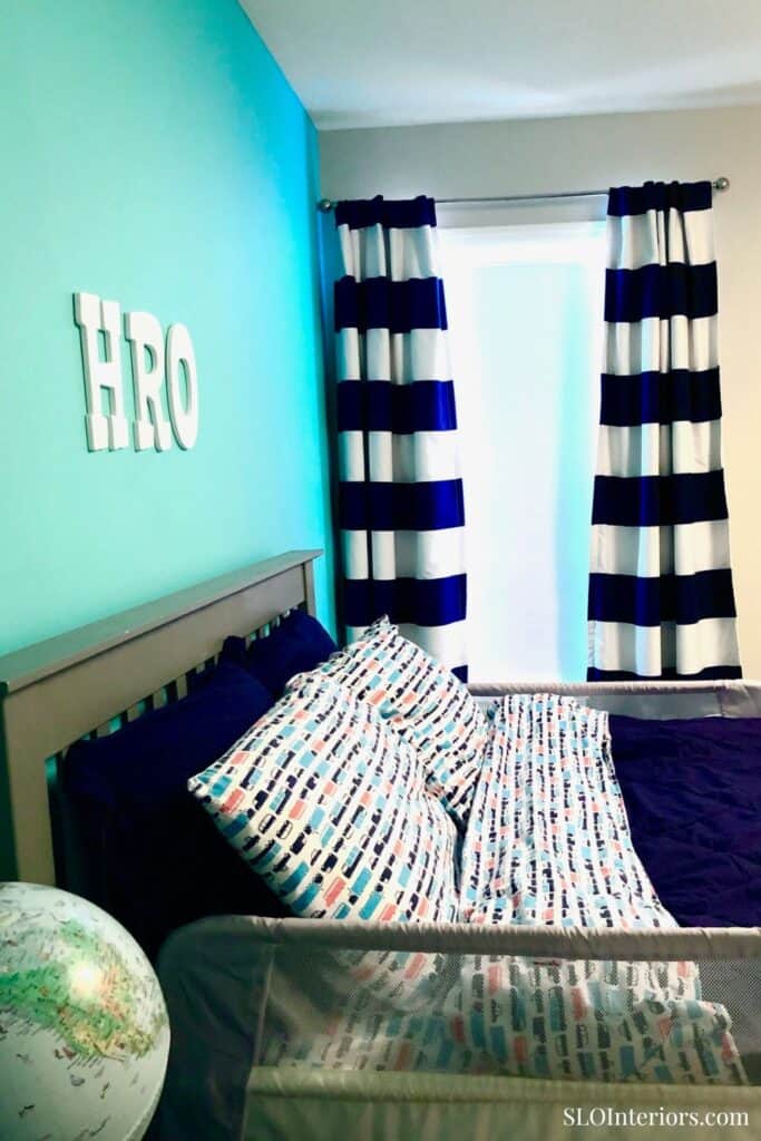 Modern bedroom with blue accent wall, striped curtains, and colorful bedding.
