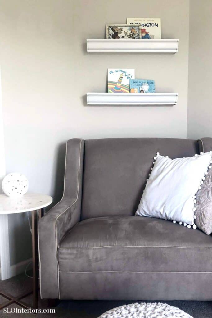Modern gray sofa with decorative pillows and wall-mounted shelves displaying books and artwork.