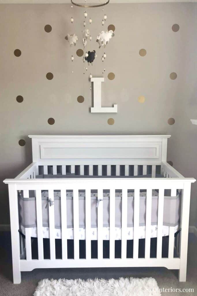 Modern white baby crib with wall decor and plush rug in nursery room.