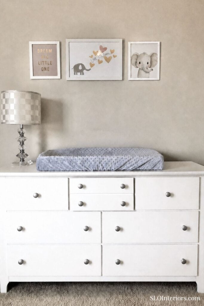A cozy nursery changing table with framed animal artwork and a soft changing pad.