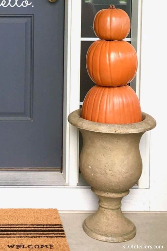 Pumpkins stacked in a decorative stone planter outside a house, autumn seasonal decor.