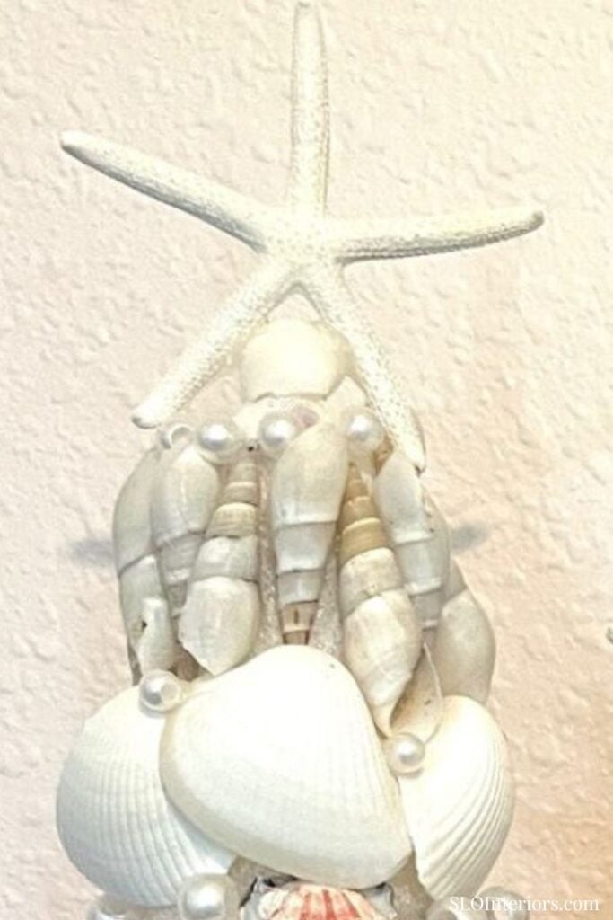 A white seashell and starfish wall decor with pearl accents and coastal theme.