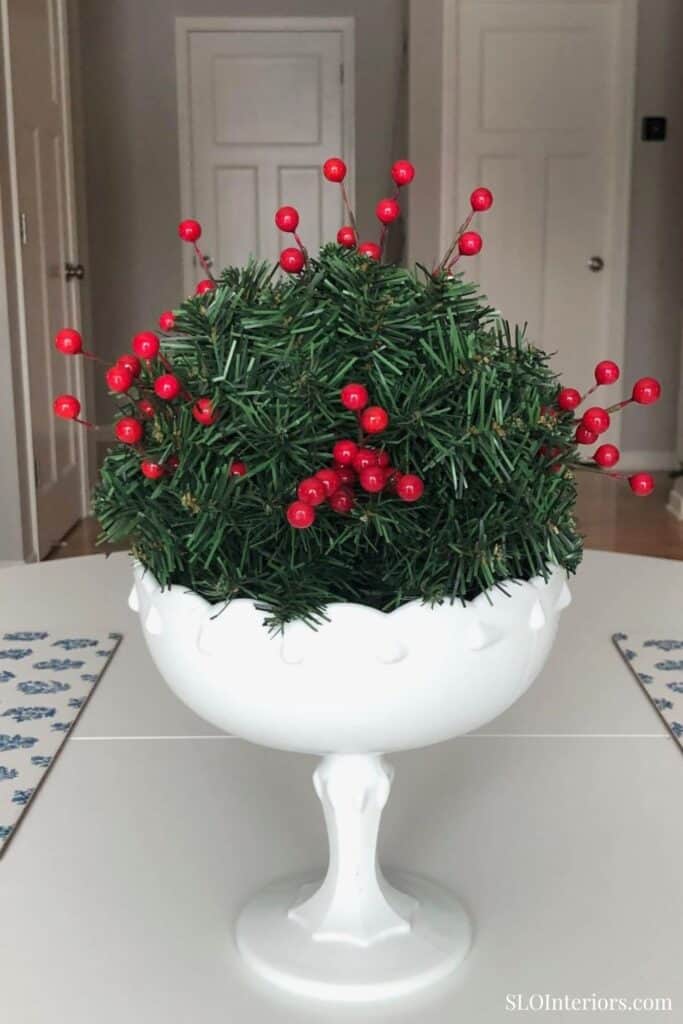 A lush holiday centerpiece with greenery and red berries in a white decorative vase.