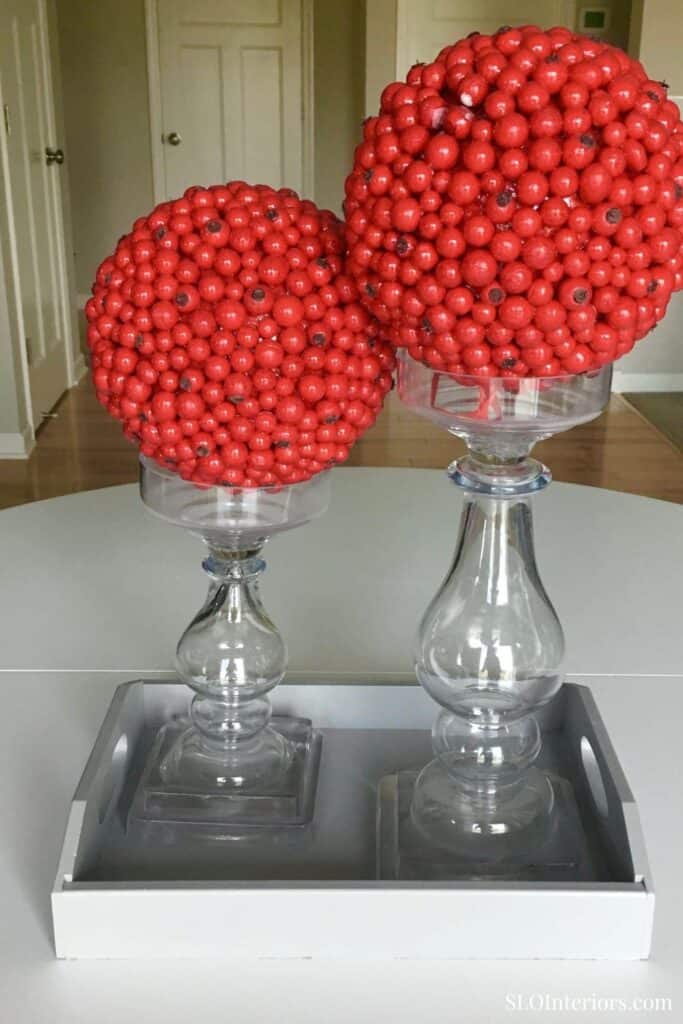 Red berry topiary decor in glass vases on tray, home interior design element.