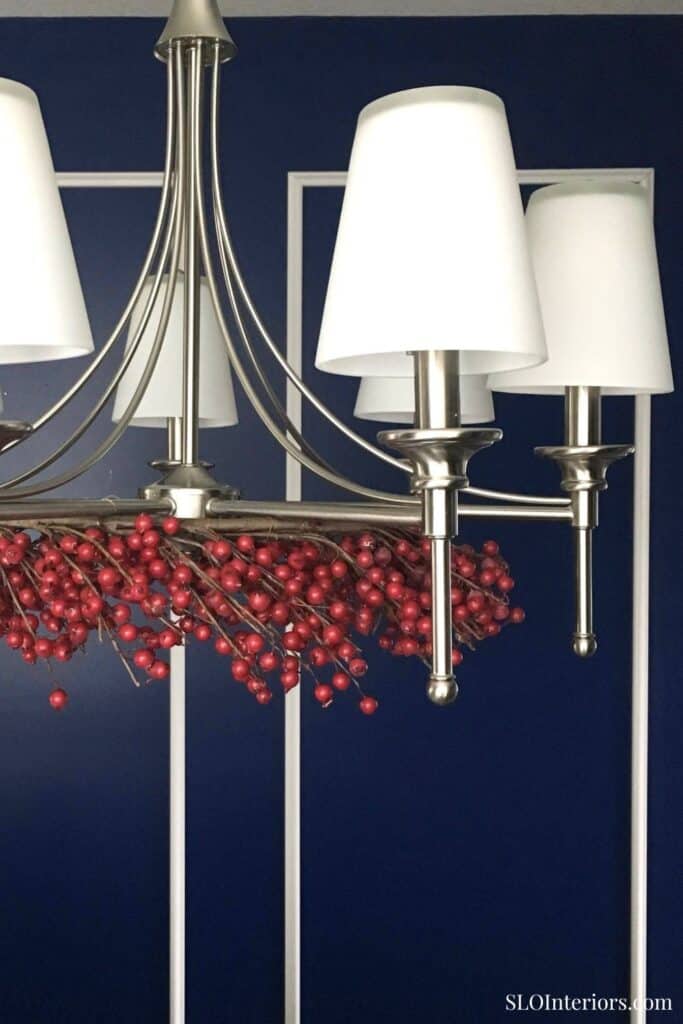 Elegant modern chandelier with white lampshades and red decorative berries against a navy blue wall.