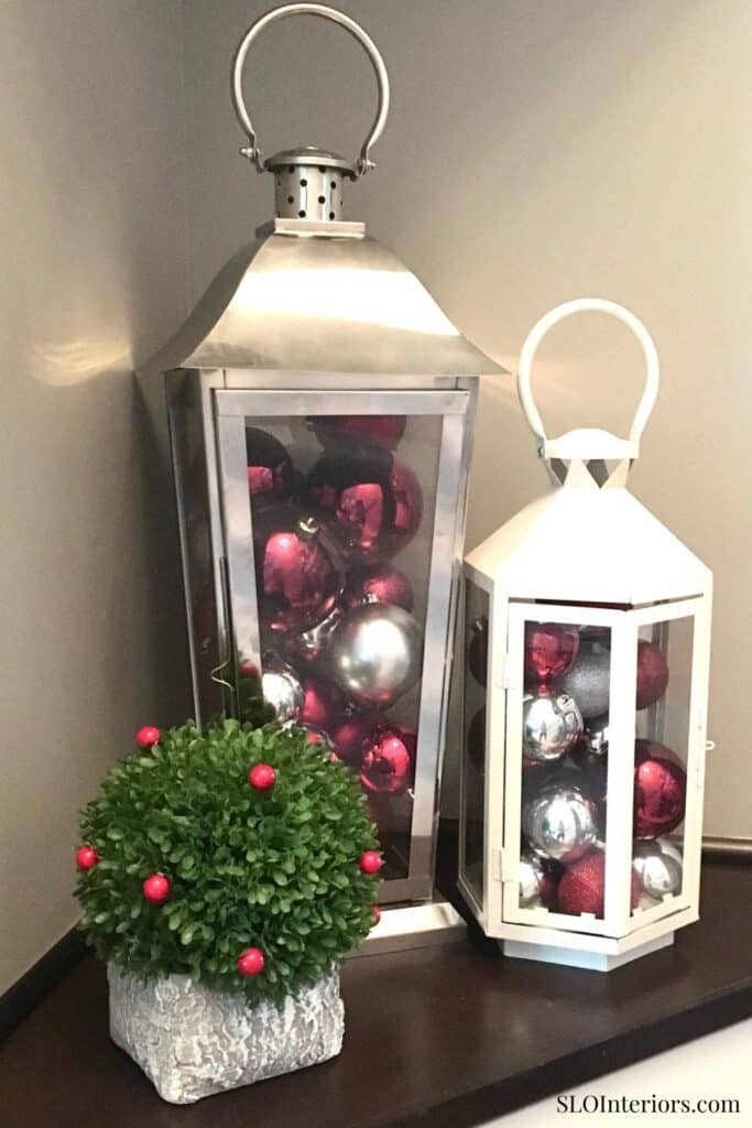 A lantern display with pink and silver Christmas ornaments and a decorative greenery arrangement.