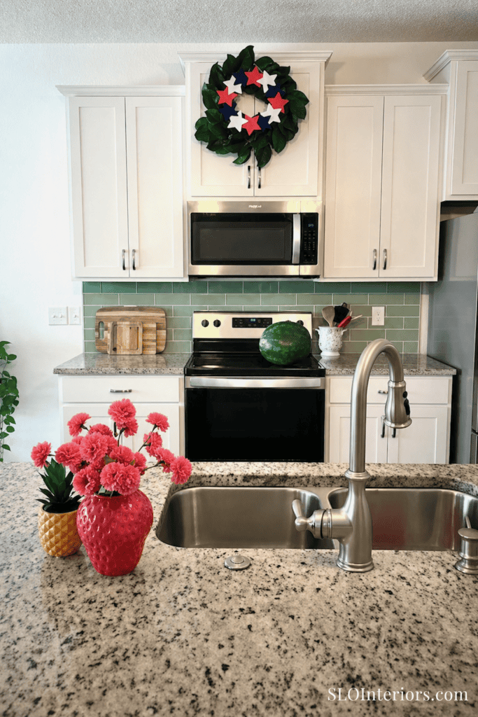 Bright kitchen with holiday wreath, watermelon, and pink flowers on granite countertop.