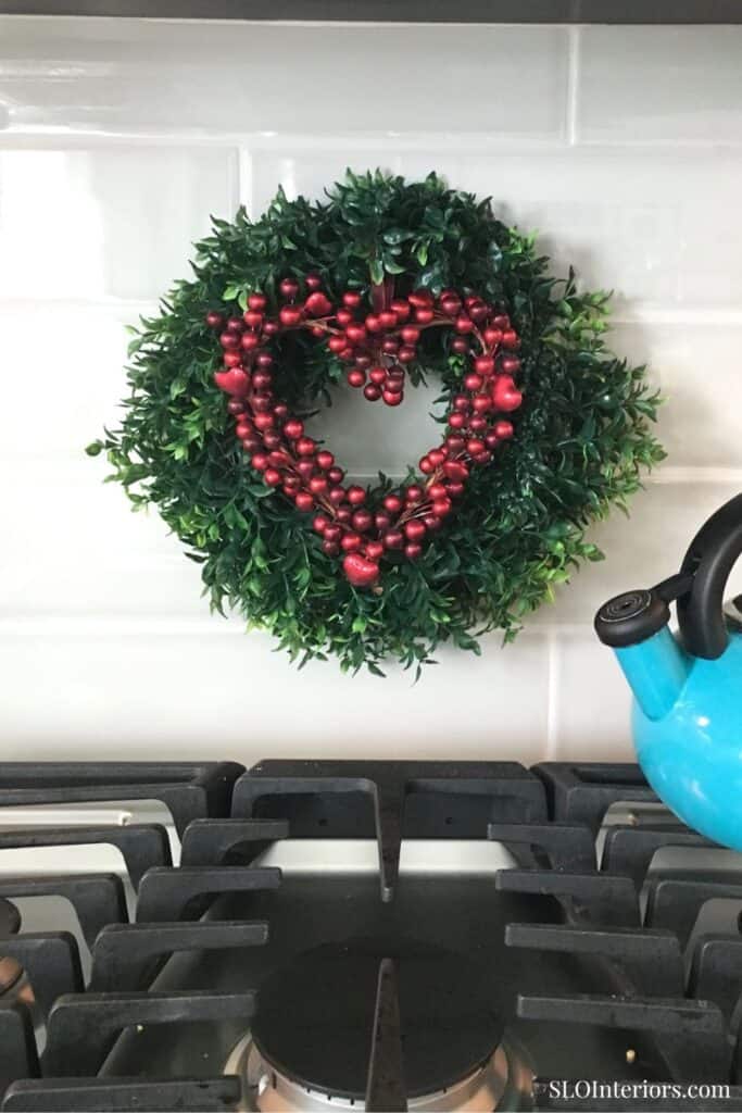 Christmas wreath with red berries and heart-shaped decoration hanging on a kitchen wall.