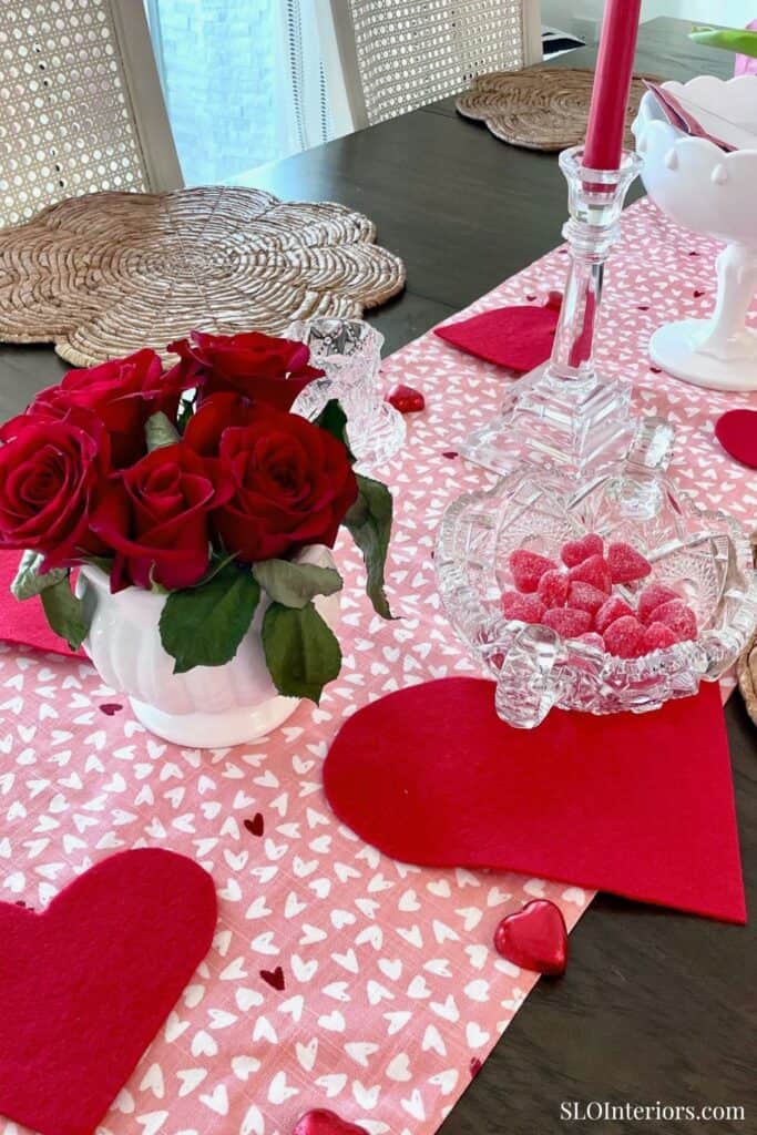 Red roses in a white vase, Valentine's Day table setting with hearts and candy, romantic decor.