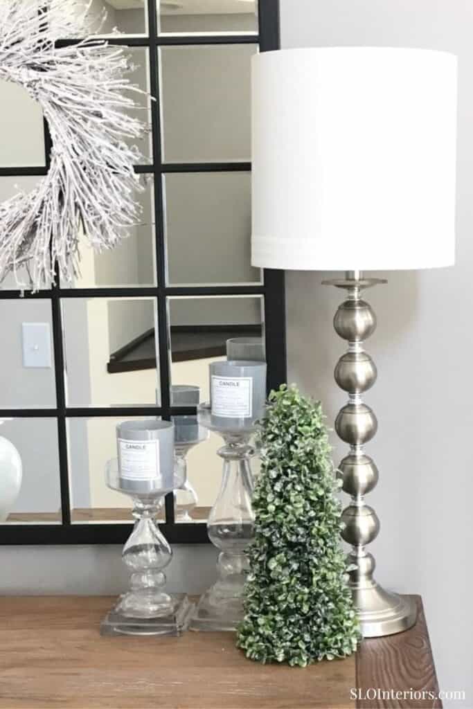 Modern table lamp with decorative candles and greenery in stylish interior setting.