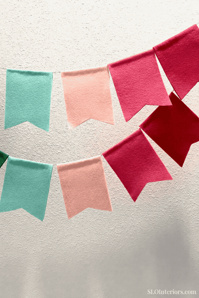 Soft pastel felt banners in mint, peach, and pink hanging on a textured wall, festive decor.