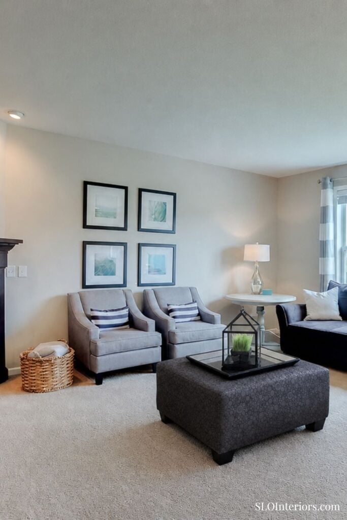 Modern living room with gray armchairs, black ottoman, and decorative wall art.