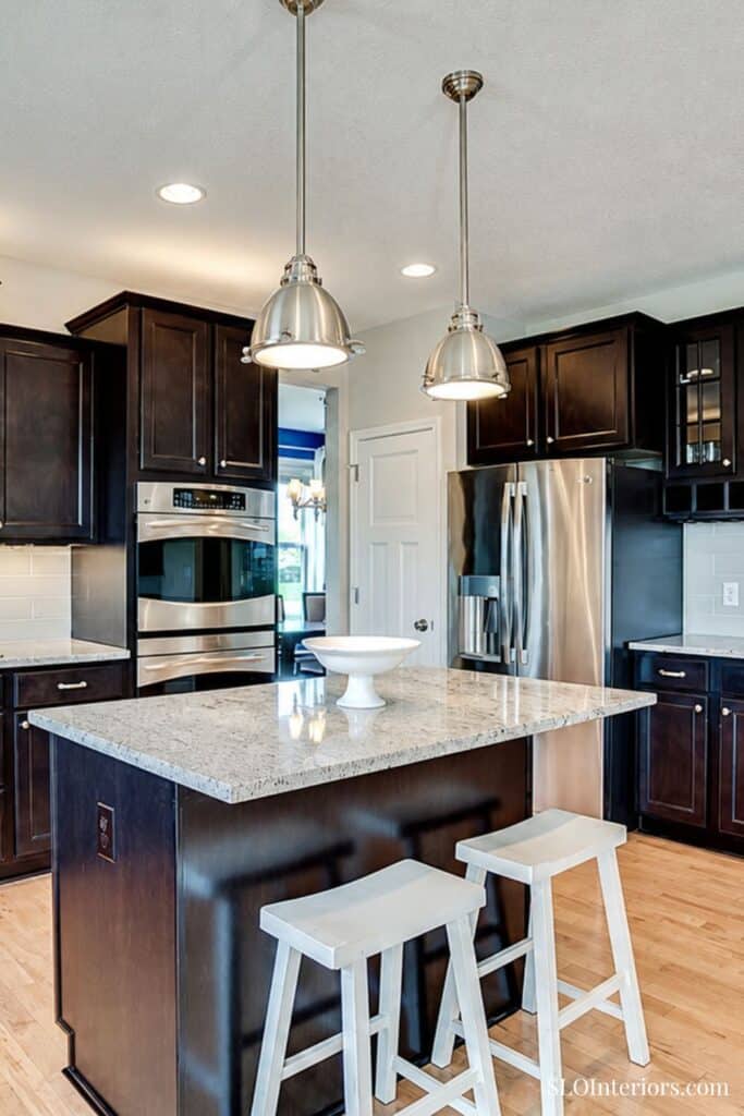 Modern kitchen with dark wood cabinets, granite island, stainless steel appliances, and pendant ligh.