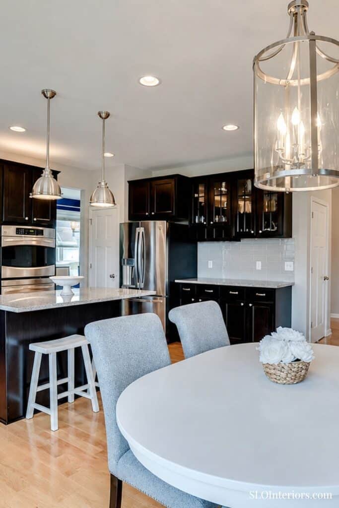 Modern kitchen with black cabinets, stainless steel appliances, and a white dining table.