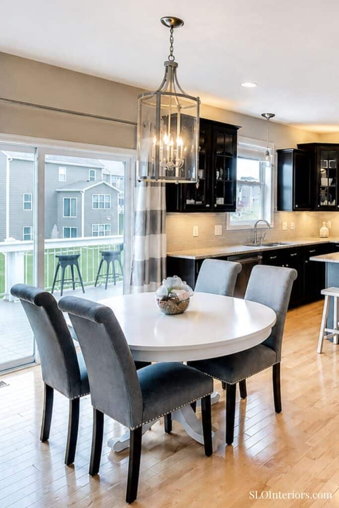 Modern kitchen and dining area with black cabinets, white table, and pendant lighting.