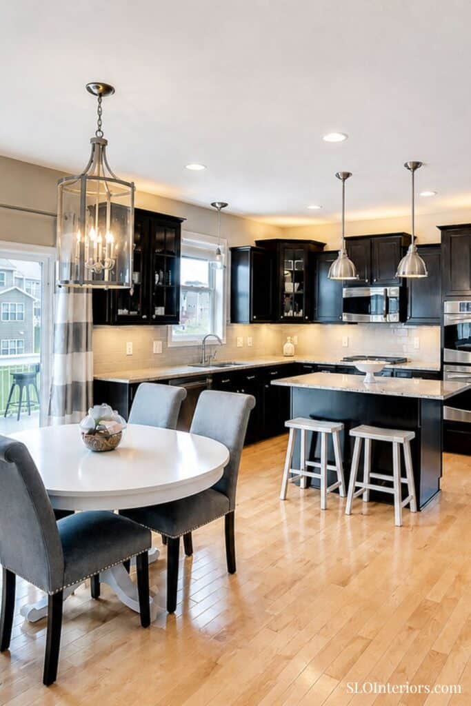Modern kitchen with black cabinets, white countertops, and dining area with gray chairs.
