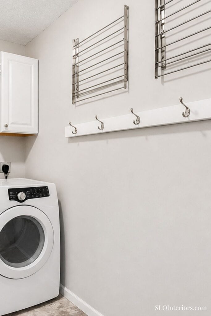 Modern laundry room with wall-mounted drying racks and hooks, white walls, and washer.