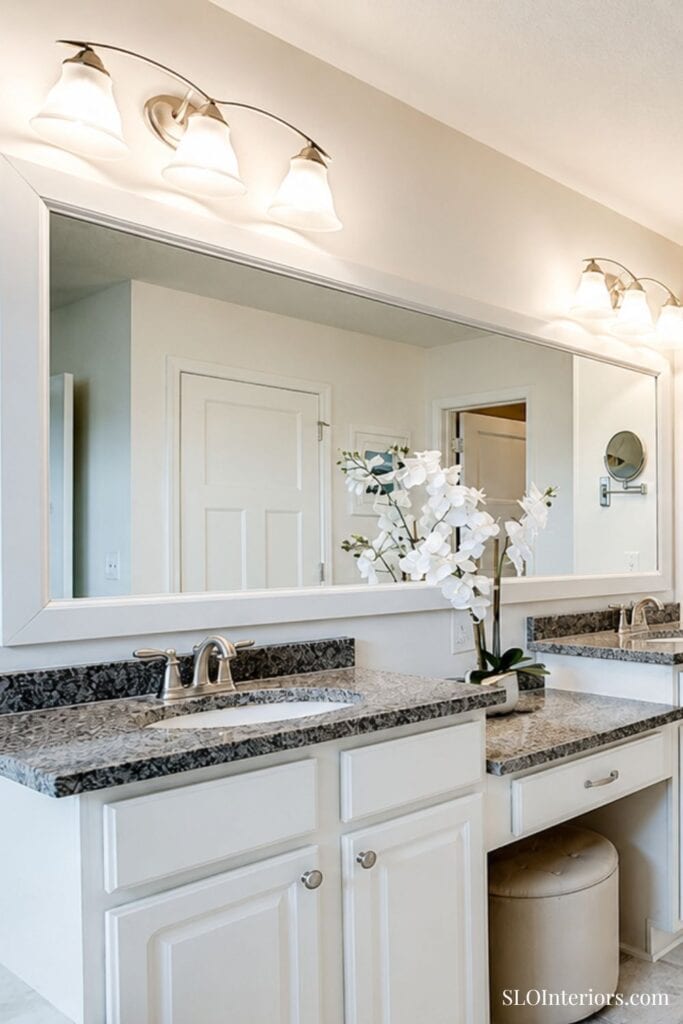 Bright modern bathroom vanity with granite countertop, white cabinets, and floral decor.