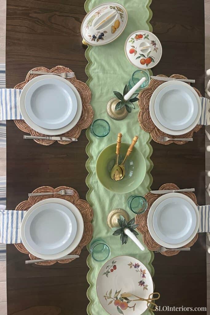 Elegant dining table setup with floral plates, green table runner, and gold utensils.