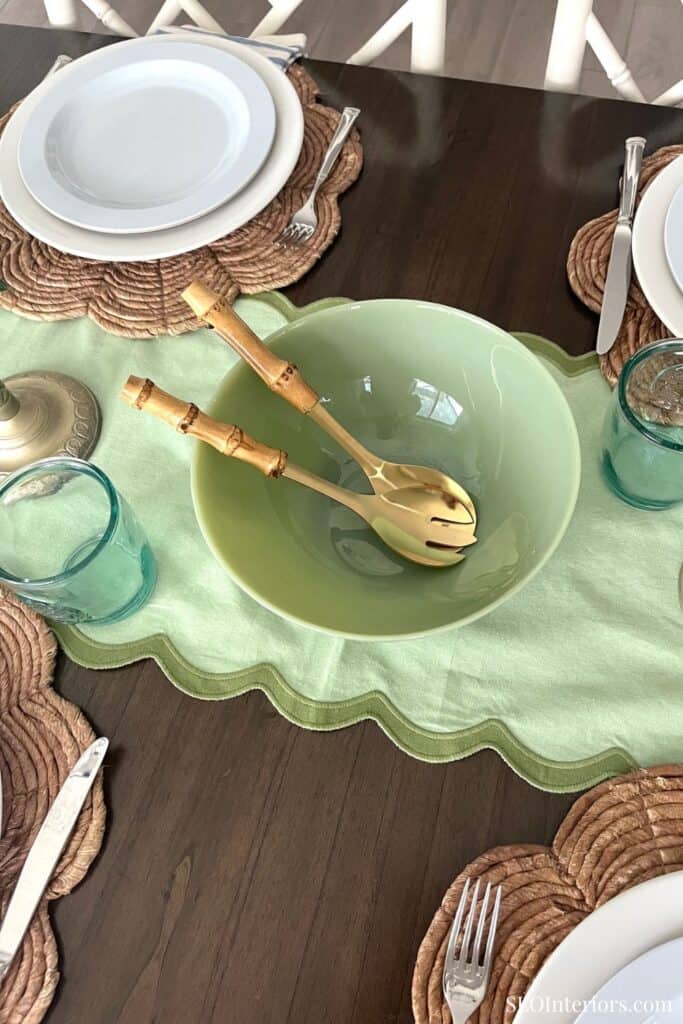 Elegant dining table setup with green bowl, gold utensils, and colorful glasses.